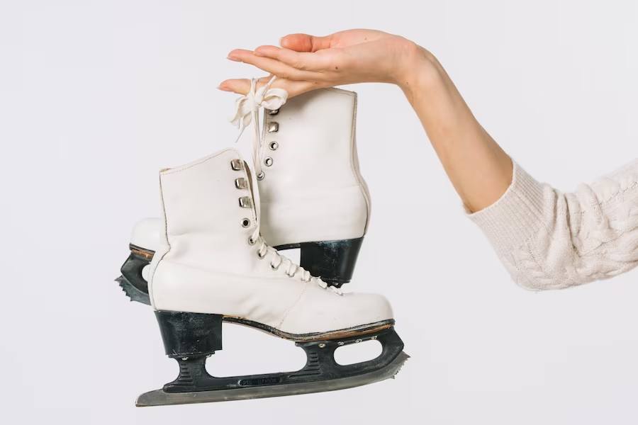 A hand holding figure skate shoes by the lace