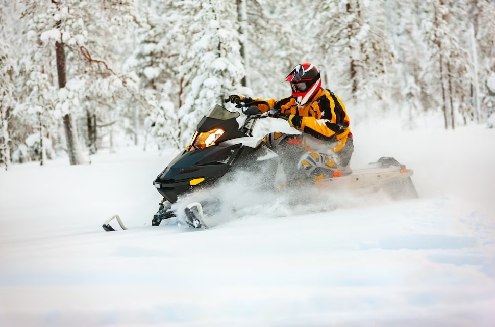 A man in a yellow-black suit and a red-black helmet, driving a snowmobile on snow