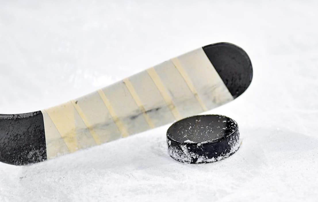 A close-up of a hockey stick blade and puck on the ice
