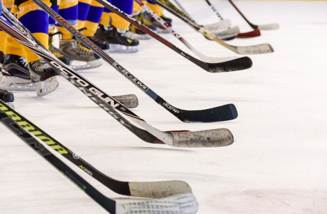 A row of ice hockey sticks on the ice with players in the background